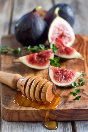 Ripe purple figs, thyme and homey on olive board. Selective focus.の写真素材