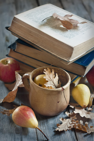 Back to school concept. Old books, apples, pears, fallen leaves and vintage mug on wooden background.の写真素材