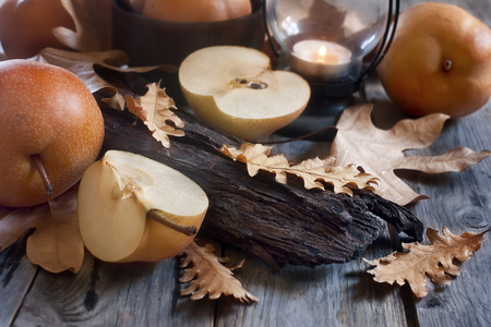 Ripe asian pears, lantern with candle and fall leaves on wooden table. Autumn concept. Selective focus.の写真素材