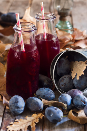 Homemade plum juice with fresh prunes and fall leaves on wooden backgroundの写真素材
