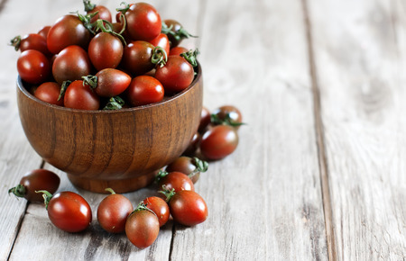 Black cherry tomato in wooden bowl. Copy space background.の写真素材