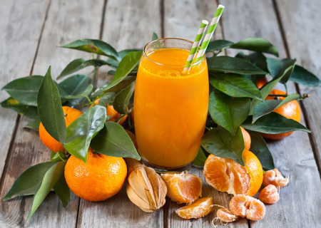 Glass of fresh tangerine juice with ripe tangerines, leaves and old-fashioned straws.の写真素材