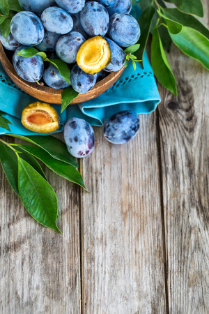Fresh plums (prunes) in wooden bowl on old wooden backgroundの写真素材