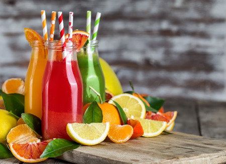 Fresh orange, blood orange juice and homemade lemonade in small bottles on old wooden table. Copy space background.の写真素材