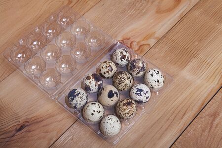 Small quail eggs in egg box on wooden background.