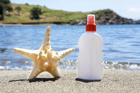 Starfish and sunscreen on the sunny sandy beach against the background of blue sea. The concept of relaxation.の写真素材