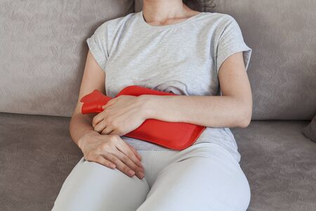 Young woman suffering from abdominal pain while sitting on bed at home. Stomach ache, women problems. Abdominal pain while sitting on bed at home.の写真素材
