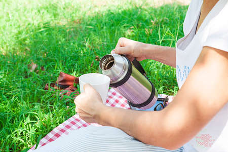 Young woman with book in hands is having a picnic in the countryside. Happy, cozy day, outdoors. Woman in park.の写真素材