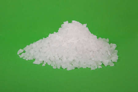 Coarse granules of natural rock or sea salt on green background.