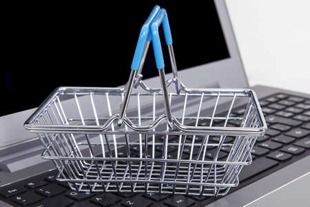 Computer and small toy shopping cart on table. Internet shopping concept.
