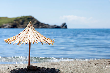 Toy sun umbrella on sandy beach on sunny day at the blue sea background. Relaxation concept.の写真素材
