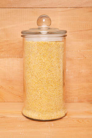 Raw, broken, organic wheat grains in glass jar on wooden background. Bulgur wheat.の写真素材