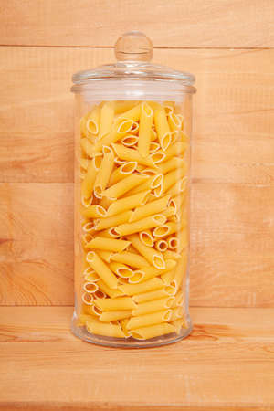 Uncooked cake in glass jar on wooden background. Pasta in the shape of a pencil.の写真素材