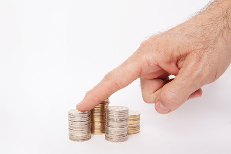 Saving money concept. The man is putting a coin into the pile of money with his hand.
