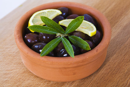 olives with leaves in a clay bowl on a wooden table.の写真素材