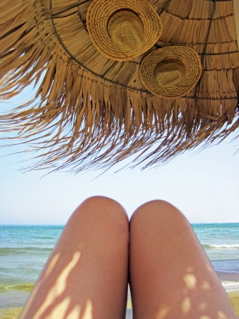            Legs of the woman sunbathing under the sunshade with 2 hats                    の写真素材