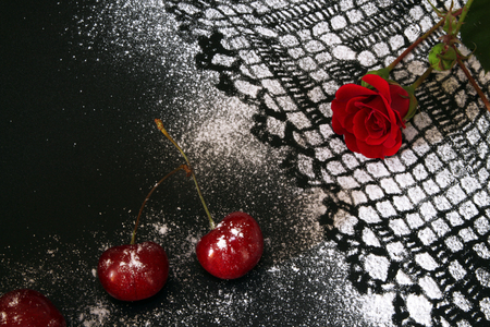 Sweet cherry against black background, lacy drawing from icing sugar and red roseの写真素材