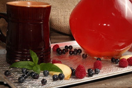 Summer fruit drinks in glass jug and ceramic cup on tray. Compot of apples, apricots, raspberry,...