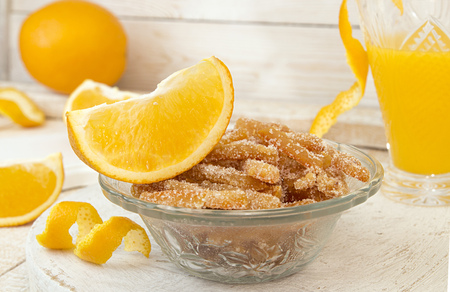 Homemade candied orange peels in glass bowl for baking fruit cake. Composition with glass of orange juice, orange fruit and orange slices on white wooden backgroundの写真素材