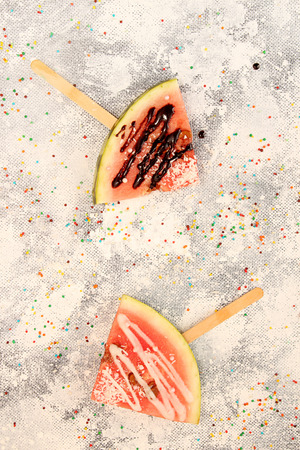 Slices watermelon in ice cream shape. Popular summer fruit watermelon with icing and chocolate on stick. Watermelon in  shape. Top view. Flat lay.の写真素材