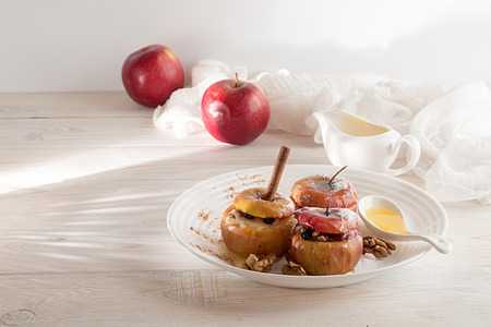Baked apples stuffed with walnuts and honey on white plate over on white wooden background. Healthy delicious sweet dessert recipeの写真素材