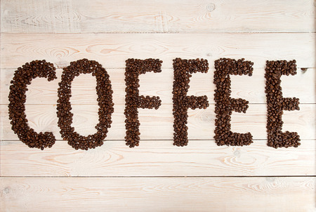 Coffee background. Heap roasted coffee beans in shape of word text coffee on white wooden background. Copy space. Top view. View from aboveの写真素材