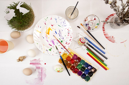 Painting Easter eggs with watercolor and markers. Paints, brushes, eggs, grass, rabbits on table