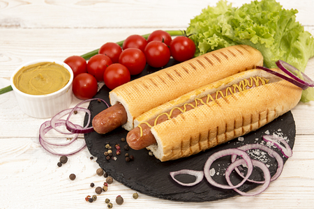Hot dogs on black slate with vegetables. Cherry tomato, pepper, lettuce, onion on white backgroundの写真素材