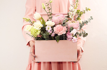 Pink wooden box with flowers roses and carnations in girl's hands on white backgroundの写真素材