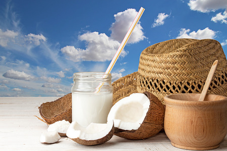 Cowboy hat, half of coconut, pieces of coconut, coconut flakes, glass jar with coconut milk on blue cloudy sky background. Travel and healthy food concept.  Copy space.の写真素材