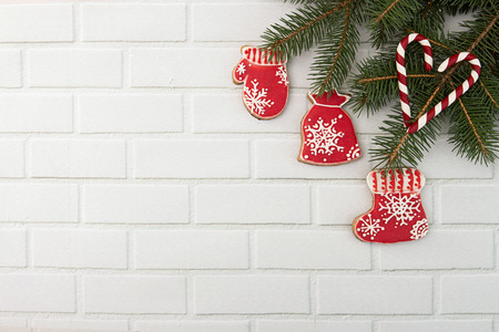Christmas New Year holiday background. Decoration with red gingerbread cookies boots, mitten, gift bag and fir branch tree against white brick wall background. Top view. Copy space.の写真素材