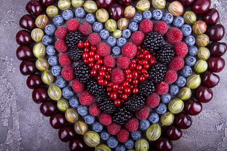 Fresh fruits and berries in heart shape over on concrete gray background. Top view. Copy space.の写真素材