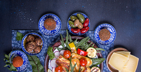 Set collection of cheese and snacks. Grilled halloumi, belper knolle, olives, tzatziki sauce over on deep blue black background. Overhead. Copy Space.の写真素材