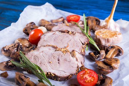 Slices of roasted meat. Cold-boiled pork with mushrooms, garlic and cherry tomato on parchment. Top viewの写真素材