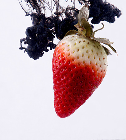 Strawberry in water. Black acrylic paint drops splashes.の写真素材