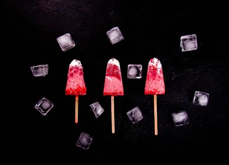 Strawberry ice cream pops with whipped cream on black background decorated with ice cubes. Top view. Flat layの写真素材