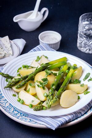 Boiled potato with grilled green asparagus on blue plate over on deep dark background. Overhead.の写真素材