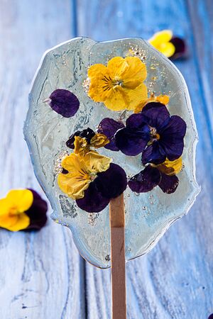 Beautiful lollipop caramel with edible violet flowers on dark blue background.の写真素材