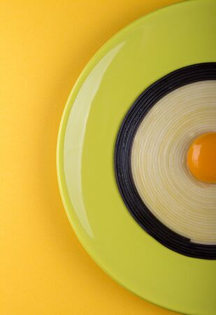 Half of olive color plate with black and white linguini pasta with egg yolk in the middle on yellow background. Top viewの写真素材