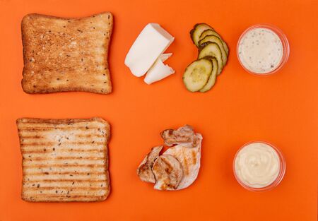 Ingredients for sandwich with chicken meat, mozzarella cheese and marinated cucumbers vegetable on trendy orange color background. Geometric Layout Ingredients composition. Top view. Flat layの写真素材