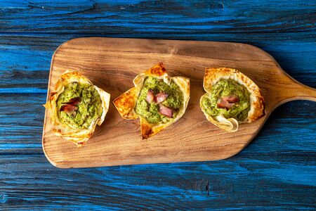 Tarts with cottage cheese, spinach, egg, mushrooms, garlic and bacon on wooden cuting board over on blue wooden background. Top view overheadの写真素材