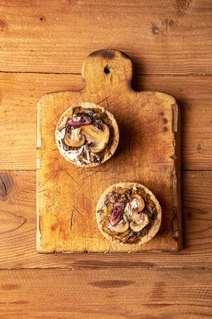 Tarts with mushrooms, caramelized red onion and cheese over on old wooden rustic background. top viewの写真素材