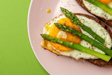 Delicious toast bread sandwiches with asparagus and fried eggs on pink plate over green background. top view, copy spaceの写真素材