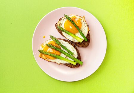 Delicious toast bread sandwiches with asparagus and fried eggs on pink plate over green background. top view, copy spaceの写真素材