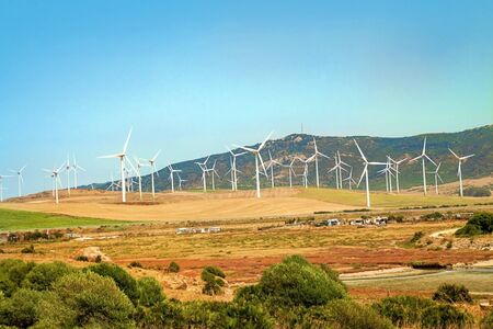 Windmills wind turbines farm power generators against landscape against blue sky in beautiful nature landscape for production of renewable green energy. Friendly industry to environment. Concept of sustainable development technology.の写真素材