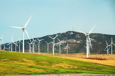 Windmills wind turbines farm power generators against landscape against blue sky in beautiful nature landscape for production of renewable green energy. Friendly industry to environment. Concept of sustainable development technology.の写真素材
