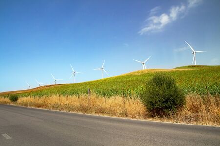 Windmills wind turbines farm power generators against landscape against blue sky in beautiful nature landscape for production of renewable green energy. Friendly industry to environment. Concept of sustainable development technology.の写真素材