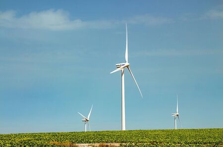 Windmills wind turbines farm power generators against landscape against blue sky in beautiful nature landscape for production of renewable green energy. Friendly industry to environment. Concept of sustainable development technology.の写真素材