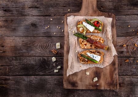 Homemade toasted bread served with green asparagus wrapped in bacon, cheese, avocado slices, grilled tomato cherry and nuts over on old rustic wooden background. Top view. Copy spaceの写真素材
