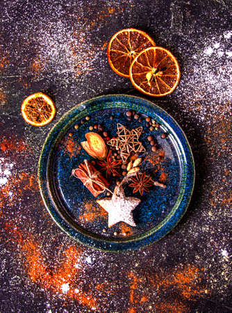 Space gingerbread. Cookie in star shape, spices, cinnamon, star anise, bell pepper, metallic star on plate over beautiful space background with dry slices of orange fruit. Top viewの写真素材